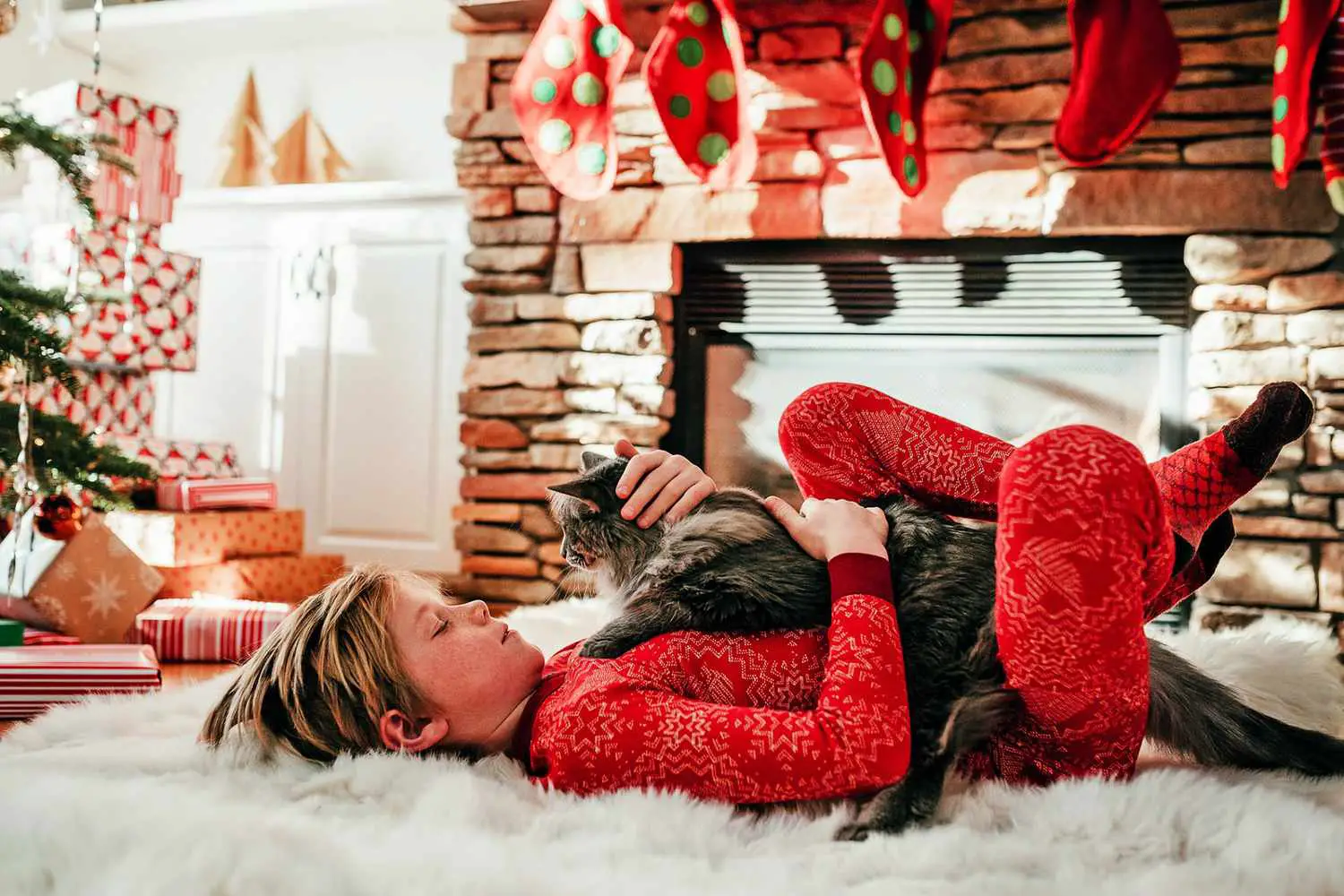 garçon allongé sur un tapis blanc moelleux avec un chat sur sa poitrine à côté d'un arbre de Noël